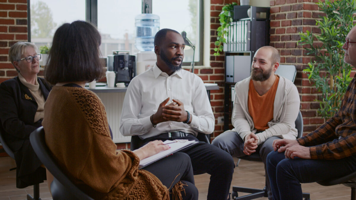 African american man sharing addiction story with group of people at aa therapy meeting